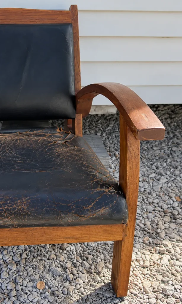 Fauteuil en chêne avant restauration, assise en cuir noir craquelé et bois terni