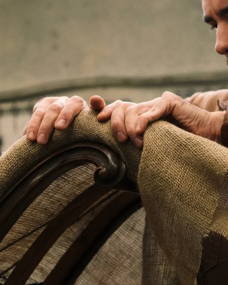 Mains d'artisan posées sur la toile de jute d'un fauteuil ancien
